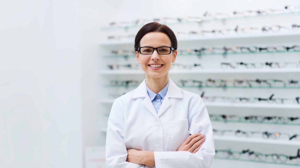 Professional optician with a welcoming smile standing before a vast array of eyeglasses, providing personalized eyewear fitting services